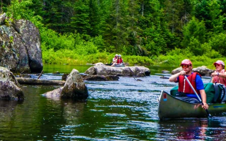two students paddle a canoe between rocks with another canoe in the background